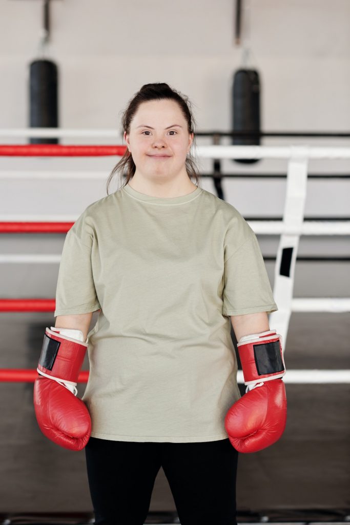 Girl with down syndrome wearing boxing gloves standing in a boxing ring smiling