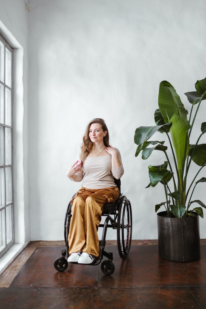 Woman on wheelchair smiling with a big plant beside her