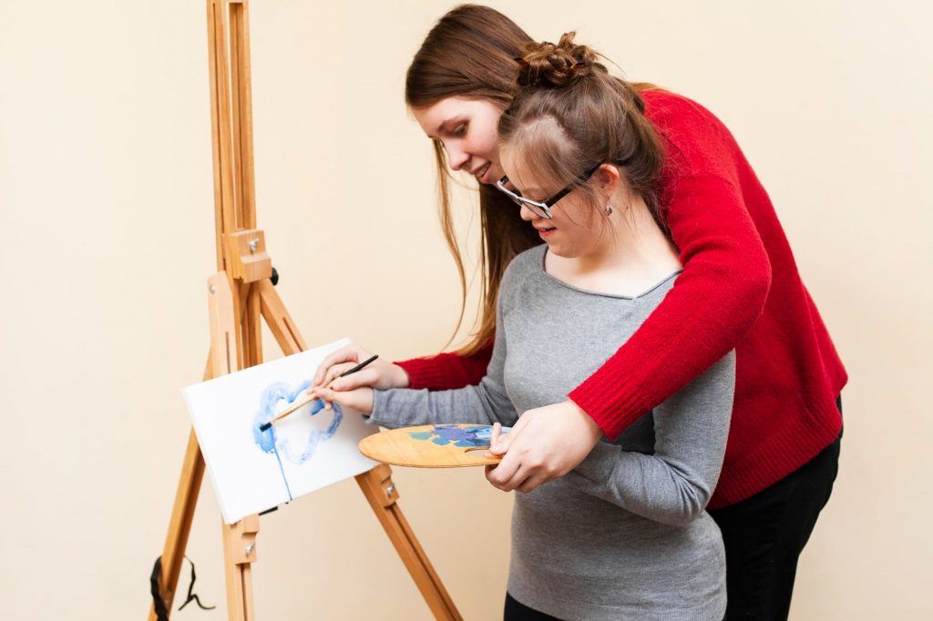 NDIS support worker helping girl with disability to paint